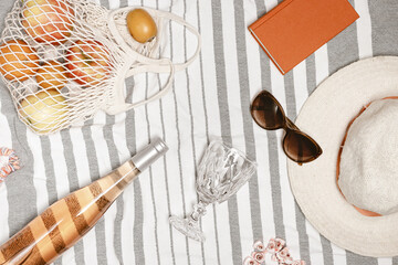 Summer holiday party, vacation, travel concept. Summer flat lay on beach towel as background. Top view bottle rose wine, wine glass, fruits in mesh bag, sun hat, sunglasses, book for reading.