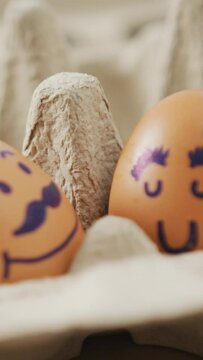 Video of close up of two brown eggs with drawn faces in egg carton background