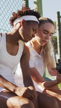 Video of diverse female tennis players using smartphone, talking and laughing