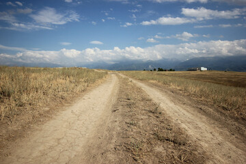 Mountain road leading over impressive highlands toward the distant, rocky, powerful mountain peak under the blue sky.