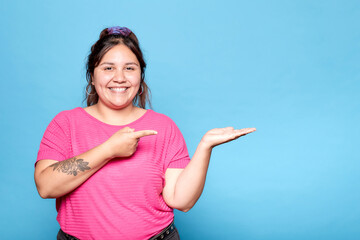 Young curvy latina woman smiling and showing copy blank space for product with open hand palm,...
