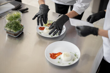 Cooks finishing main courses, putting greens on plates with rise and meat, close-up on table with...