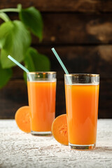 pumpkin juice with orange, orange juice in a glass, fresh vegetable juice in a transparent glass, two glasses on a wooden table, wooden table and green leaves, sun rays