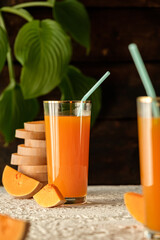 pumpkin juice with orange, pouring juice into a glass, human hand, two glasses with juice on a concrete table, sun rays, creative photo of a drink for a magazine, space for text