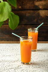 pumpkin juice with orange, orange juice in a glass with a straw, fresh vegetable juice in a transparent glass, two glasses on a concrete table, gray concrete table and green leaves, sun rays