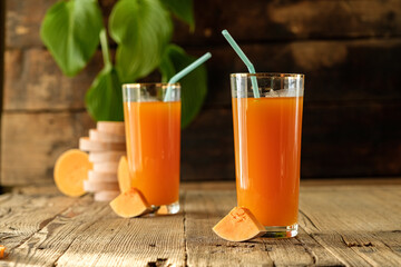 pumpkin juice with orange, orange juice in a glass, fresh vegetable juice in a transparent glass, two glasses on a wooden table, wooden table and green leaves, sun rays