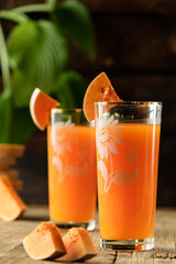 pumpkin juice with orange, orange juice in a glass with a straw, fresh vegetable juice in a transparent glass, two glasses on a concrete table, gray concrete table and green leaves, sun rays