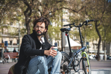 Fototapeta premium Young man sitting on the bench holding cup of coffee