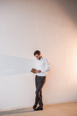 A man standing by the white wall, reading a book