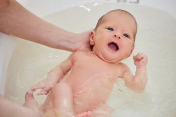 mother bathes her baby in a white small plastic tub