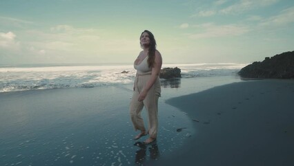 Happy plus size girl with long hair walking on the black sand beach. Body positivity. 4K