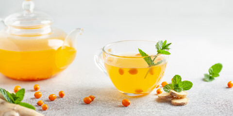 Hot autumn tea with sea buckthorn, ginger and mint in a glass teapot on a gray background