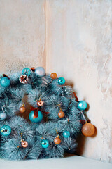Round fir garland with snow, blue glitter balls and pine cones. Traditional Christmas decorative wreath over grey marble wall. Holiday interior details. Copy space for New Year congratulations.