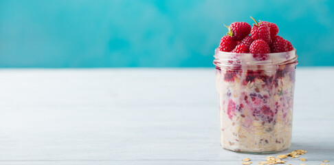 Overnight oats, bircher muesli with fresh raspberries in a glass jars on wooden table. Copy space.