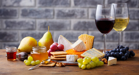 Assortment of cheese, grapes with red and white wine in glasses. Stone and wood background. Close...