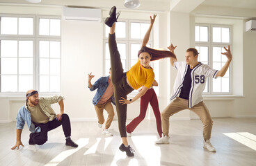 Group of young people dancing together. Contemporary dancer practising dance moves. Flexible girl doing a standing leg split tilt with one leg up while rehearsing with her friends in a modern studio