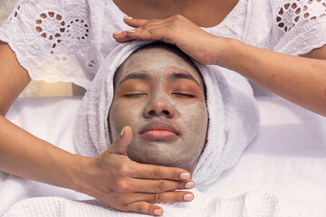 Fototapeta na wymiar African American woman lying creamy facial mask and relax and have a facial massage with a facial massage technician wearing a facial mask by the pool spa resort.Wellness and beauty health concept.