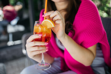 Young girl holding an aperol spritz. Cocktail aperol spritz in a glass. Young girl in a restaurant...