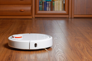 White robotic vacuum cleaner on laminate wood floor in living room. Shallopw focus.