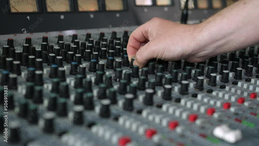 Poster recording studio engineer turning a knob on a mixing desk console