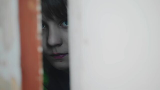 The boy looks out fearfully through the crack between the doors. He looks warily at the camera. Close-up