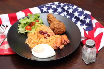 American fried rice served with sausages, cucumbers, shredded vegetables in a gray plate on a white table with seasoning.