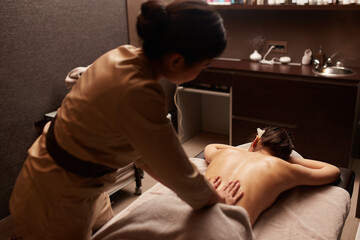 Rear view of a masseuse gives a body massage to a young woman. Spa relaxation concept.