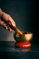 a hand with a hammer and a Tibetan bowl on a dark background