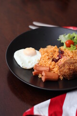 American fried rice served with sausages, cucumbers, shredded vegetables in a gray plate on a white table with seasoning.