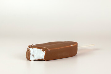 Chocolate ice cream bar with stick. Melting and broken chocolate popsicle on pastel color background. Refreshing Summer dessert close up image.