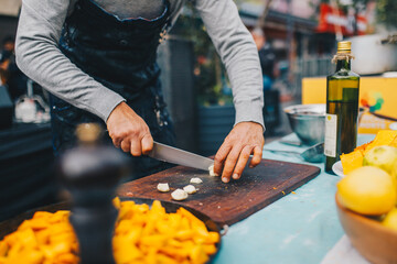Chef hombre picando ajo en una tabla de madera - obrazy, fototapety, plakaty