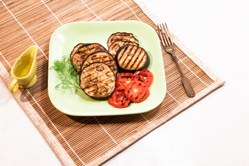 Grilled eggplants and tomato in plate on white background.
