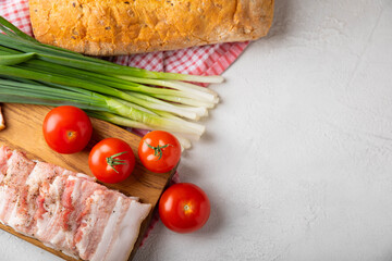 Board with pork fat, green onions, homemade bread and cherry tomatoes on a gray stone background....