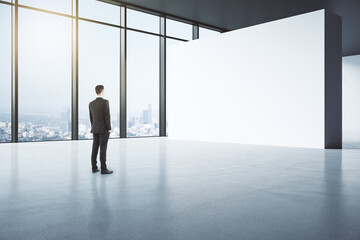 Perspective view businessman in black suit back view looking at blank light partition in empty...
