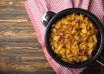 Braised pork with potatoes and onions on a brown textured wood. Copy space. Place for text. Fried potato recipe.