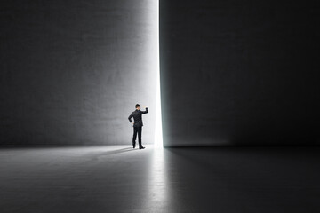 Business success and look into the future concept with businessman looking through a light hole in a dark wall in empty spacious hall