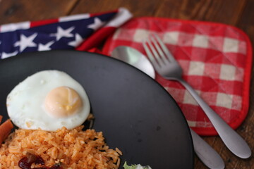American fried rice served with sausages, cucumbers, shredded vegetables in a gray plate on a white table with seasoning.