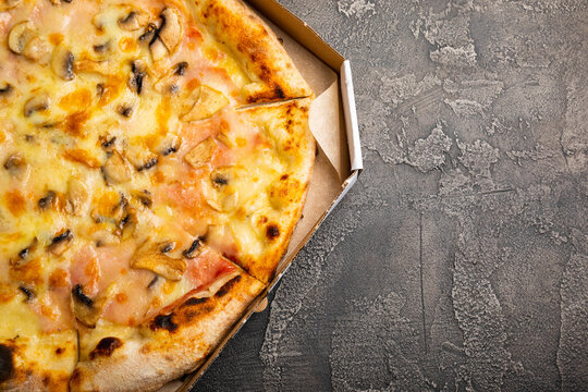  Tasty Italian pizza with vegetables and sausages in a box on a black marble background. Side view. Place to copy.