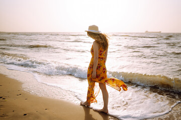 Fototapeta na wymiar Beautiful woman in summer dress and hat walking on the beach. Travel, weekend, relax and lifestyle concept.