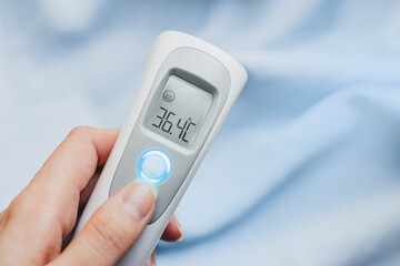 Hand holding ir thermometer with normal temperature. Medical office measurement product. Healthcare...