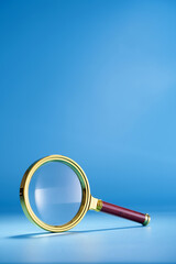 gold colored frame of magnifying glass wth red handle against blue background