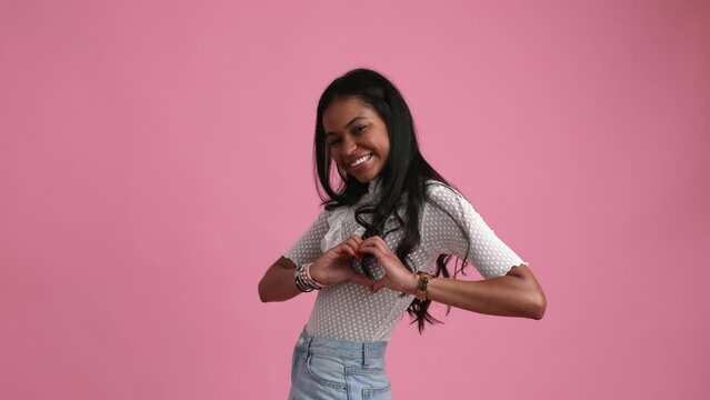 Happy young black woman in her 20s smiles and shows her heart sign on her chest.