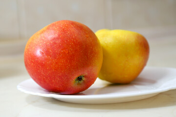 Two ripe red and yellow apples on the white plate