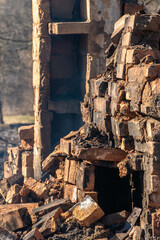 Fototapeta na wymiar Destroyed houses as a result of a fire in Russia. An old brick rustic stove covered with ash and partially destroyed after a severe fire in a wooden house. Natural disaster