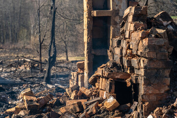 Fototapeta premium Destroyed houses as a result of a fire in Russia. Bricks and parts of walls, various household items, broken windows covered with ash lie on the surface of the earth. Natural disaster