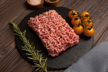 Minced meat on a cutting board with a sprig of rosemary, cherry tomatoes, pink salt and a mixture of peppers on a wooden background, flat lay, open space