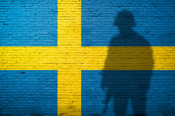 Flag of Sweden painted on a brick wall with soldier shadow