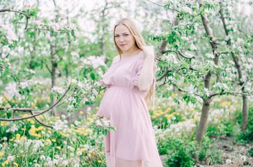 Pregnant girl in a pink dress in a flower garden