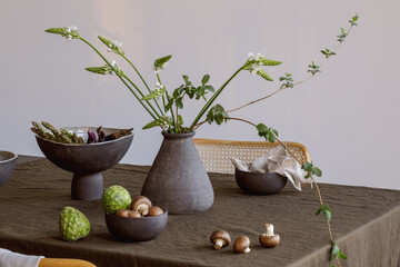 Elegant table setting with green brunches in craft vase , cherimoya fruits, brown champignons, eggplants in craft ceramic plate on linen tablecloth. Outdoor table setting for summer holiday concept.