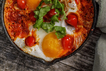 Homemade Shakshuka served  in a Frying Pan. Eggs Poached in Spicy Tomato Pepper Sauce.  Fried eggs, onion, bell pepper, tomatoes and parsley in a pan on aged wood background